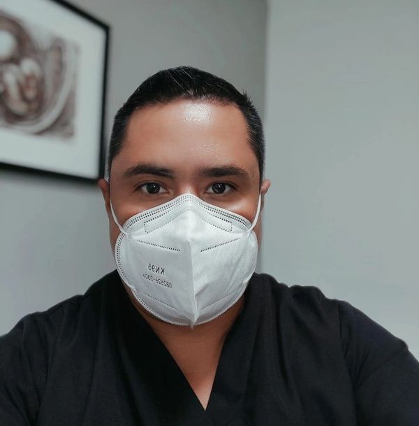 Man wearing a white KN95 face mask and black shirt indoors.