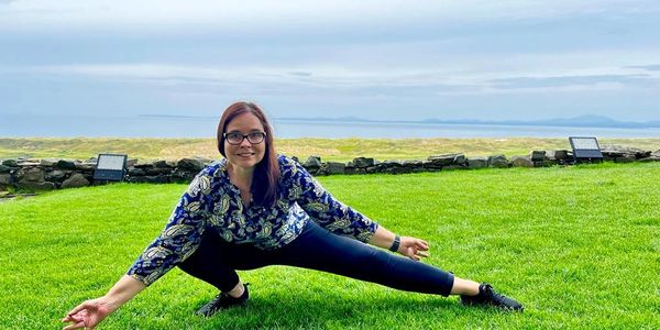 Angela doing a half yogi squat (Ardha Malasana)  outdoors on the grass