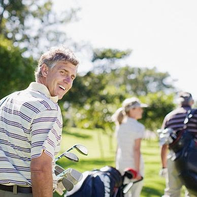 young male golfer facing camera holding golf clubs with a lady and man in the background