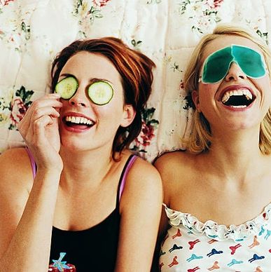 two young ladies lying down, laughing with cucumbers and cold mask on eyes