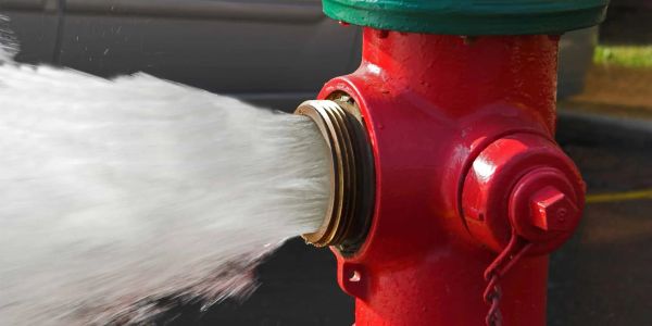 Water forcefully flowing out of a red fire hydrant.