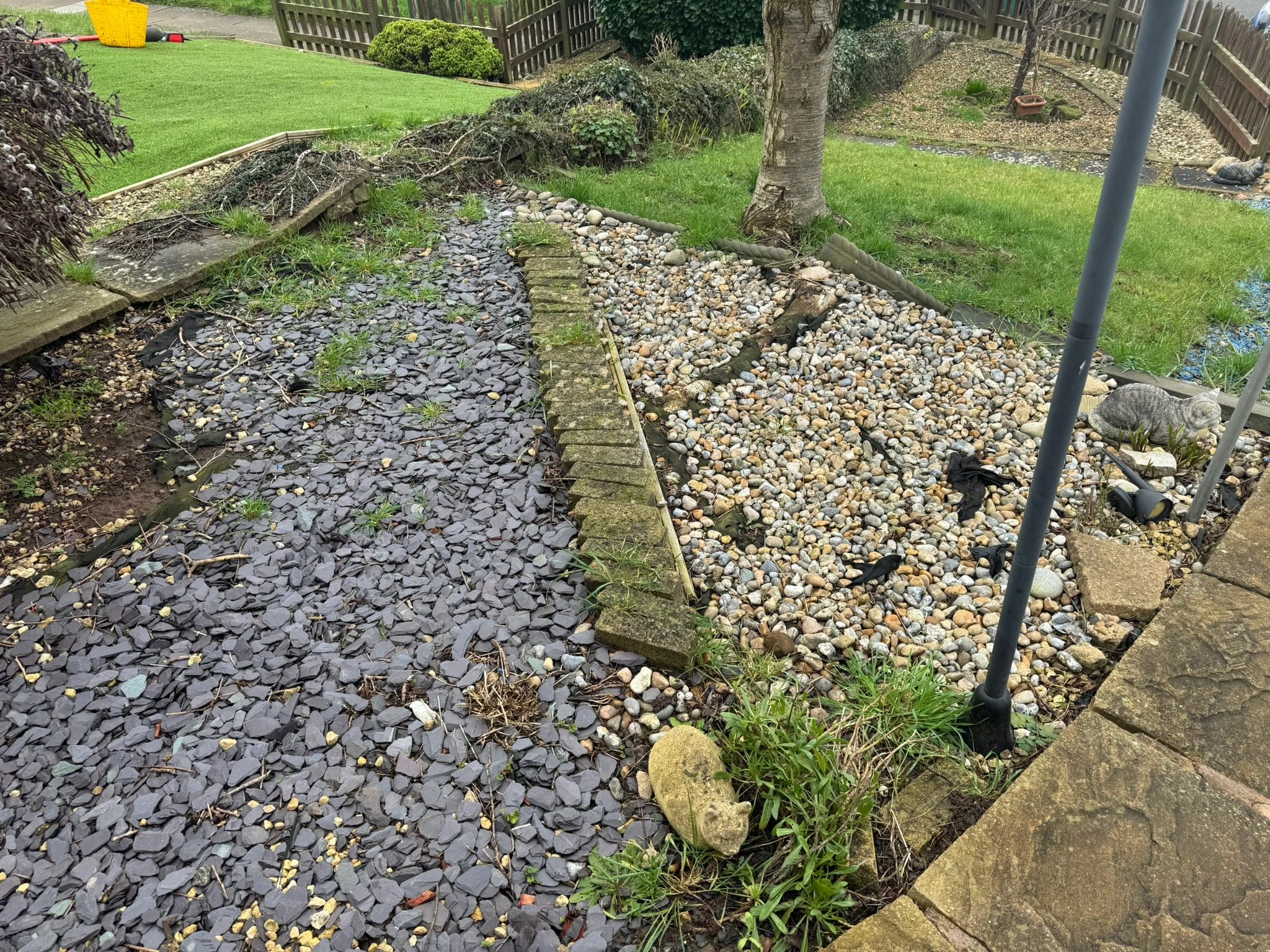 Garden with pebbles, slate, and decorative statues near a tree.