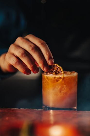 Man garnishing a mixed drink with an Orange