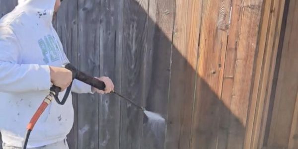A&R Bentley Painting crew member spray-applying stain sealant to a backyard wood fence