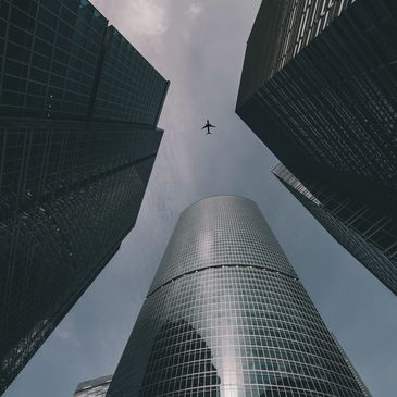Airplane flying above tall skyscrapers.