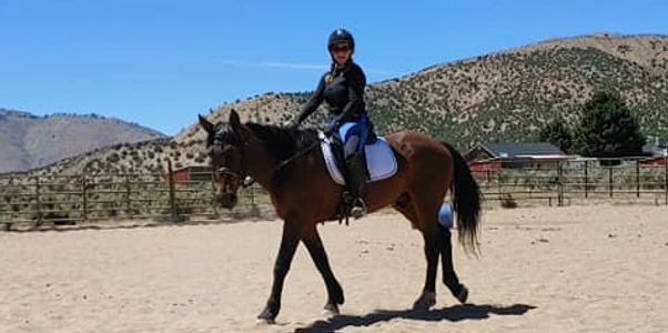 happy woman riding a bay horse in dressage tack in an arena