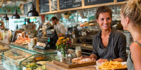 Nowoczesna kawiarnia, uśmiechnięta obsługa przy ladzie, świeże pieczywo i frytki, ciepła, przyjazna 
