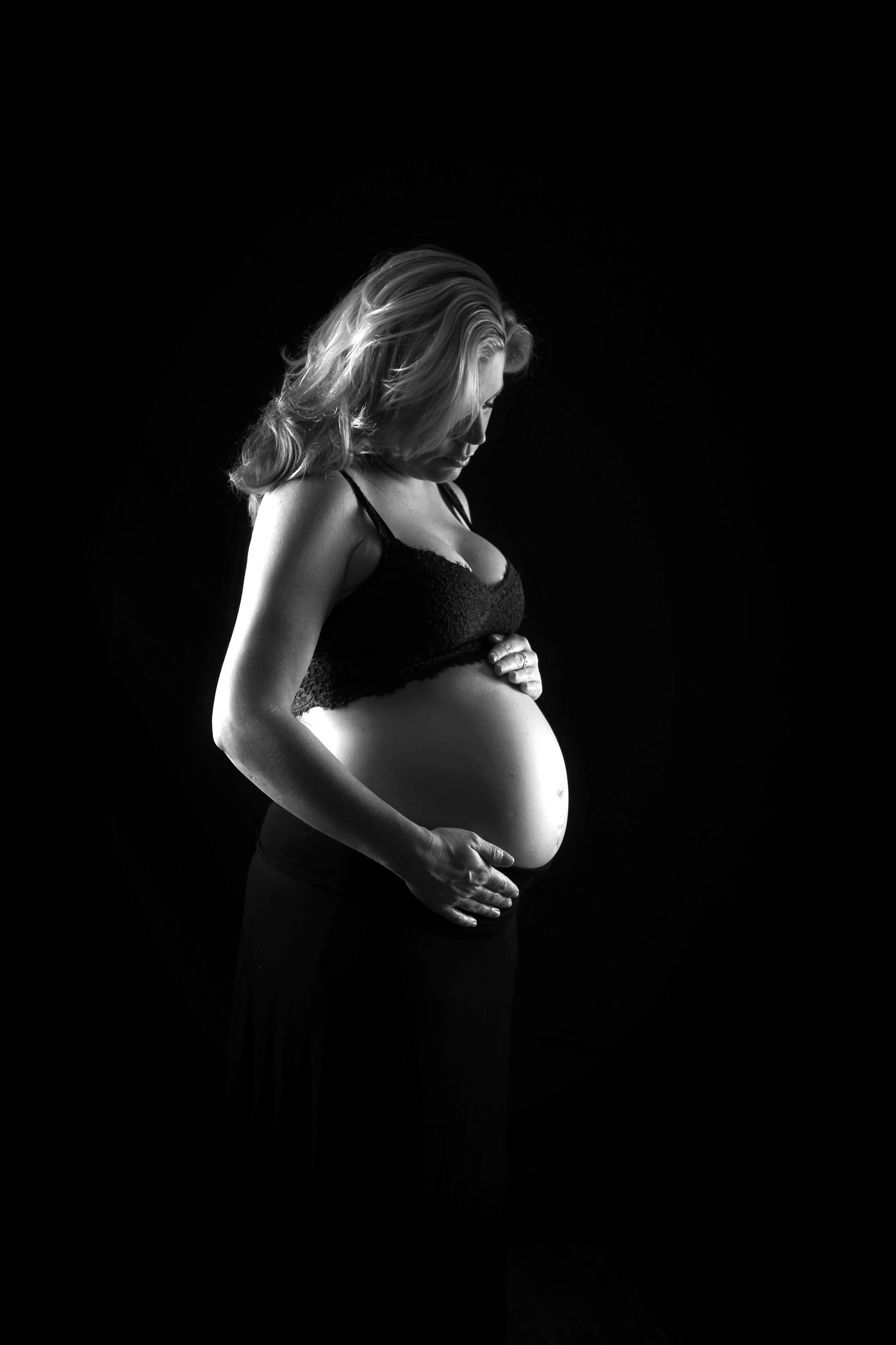 Black and white portrait of a pregnant woman gently holding her belly.