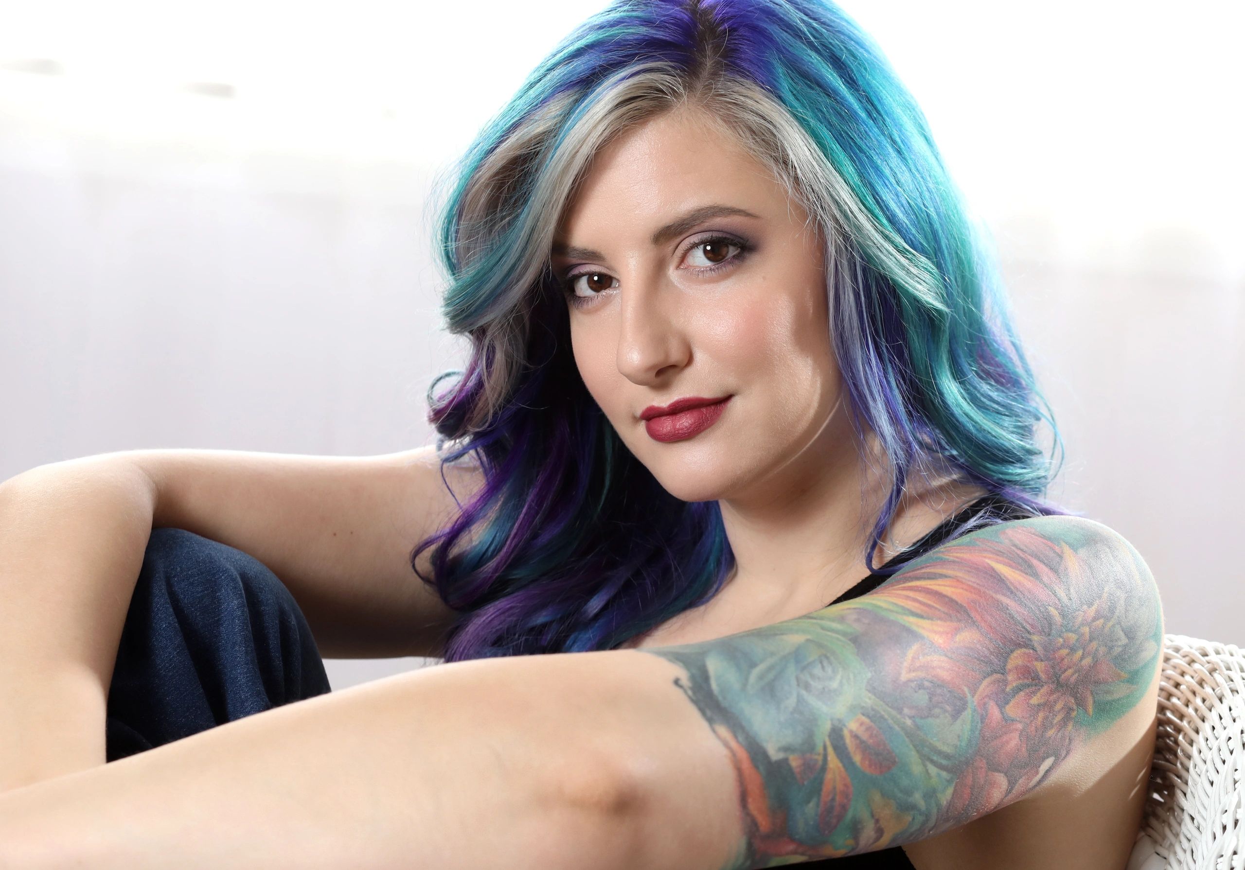 Young woman with vibrant blue and purple hair and a colorful floral tattoo on her arm.