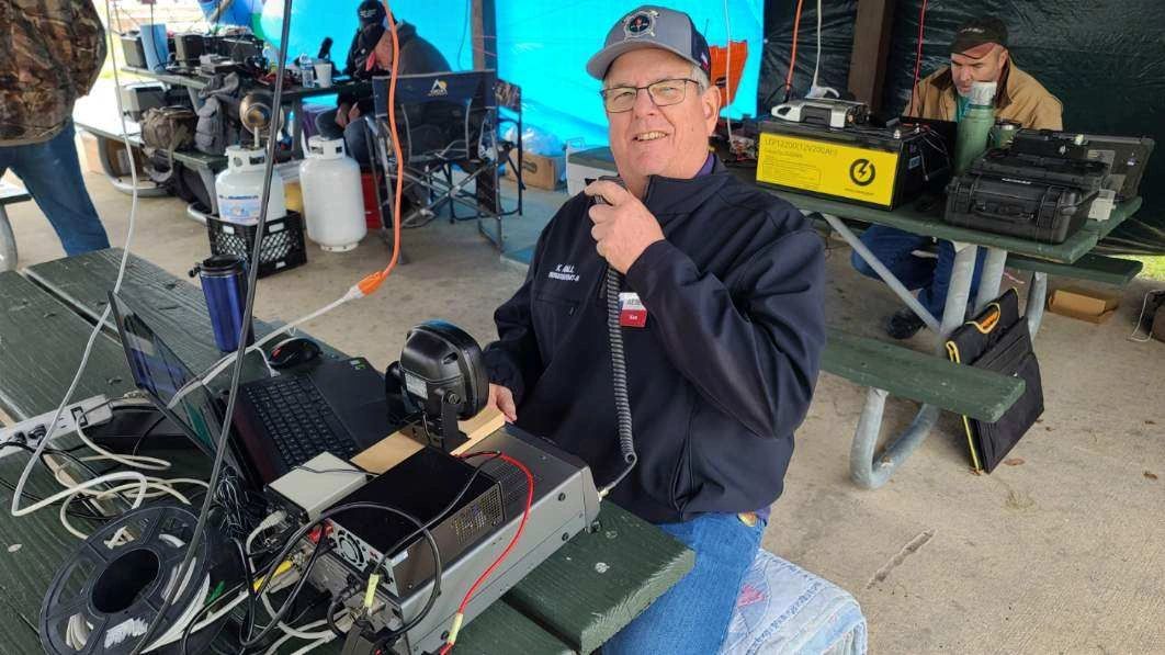 Man using radio equipment at an outdoor setup under a tent.