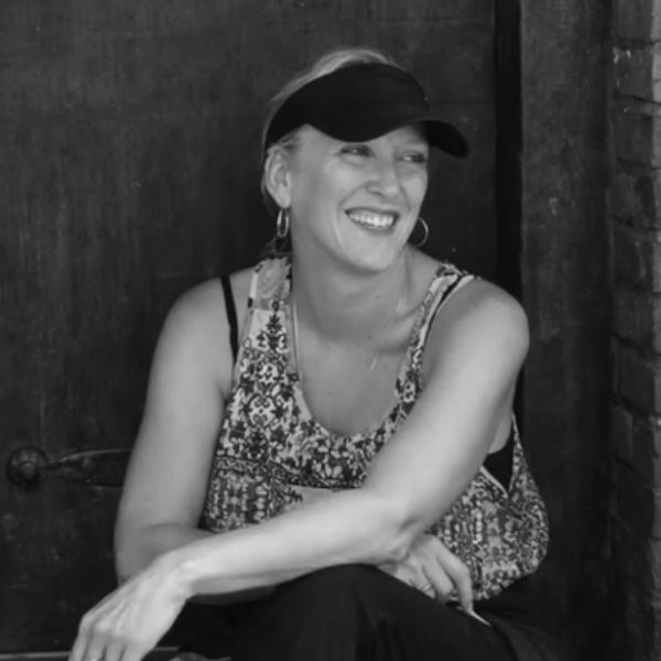 Smiling woman in a visor and patterned top sitting relaxed against a dark background.