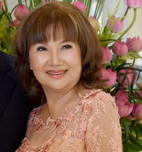 A smiling woman in a peach lace dress with flowers in the background.