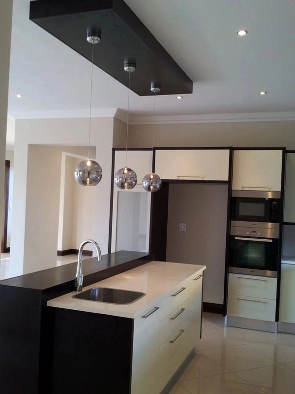Modern kitchen with sleek black and white design and hanging spherical pendant lights.