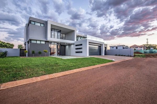 Modern two-story house with large windows and a well-maintained lawn at dusk.