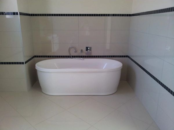 A modern white bathtub in a tiled bathroom corner with black border accents.