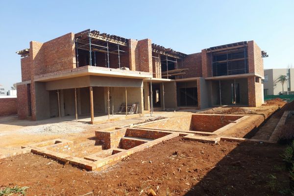 Under-construction two-story brick house with foundation and scaffolding.