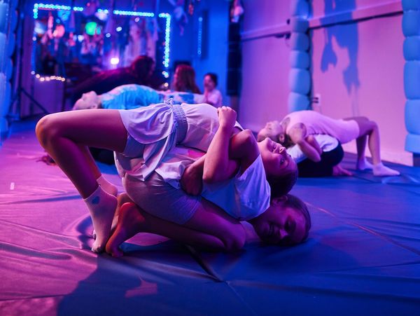Children practicing acro yoga in a dimly lit room with blue and purple lights.