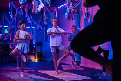 Children practicing yoga poses in a dimly lit, colorful studio.