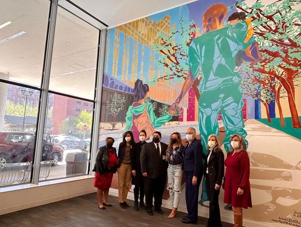 Group of people posing in front of a colorful mural indoors.