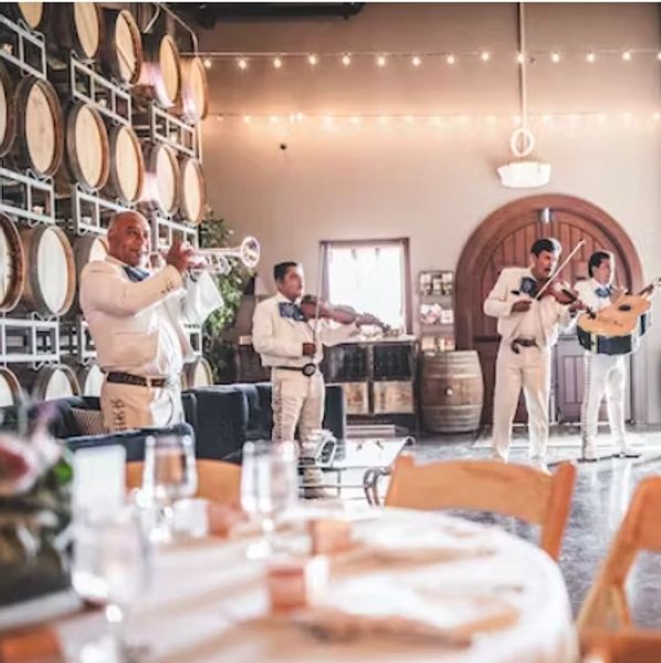 A mariachi band plays in a warmly lit room with wine barrels.