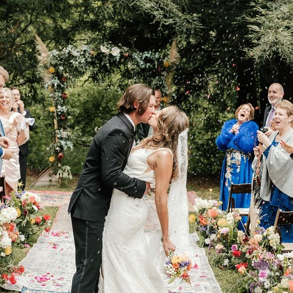 Bride and groom share a kiss at outdoor wedding ceremony surrounded by joyful guests.