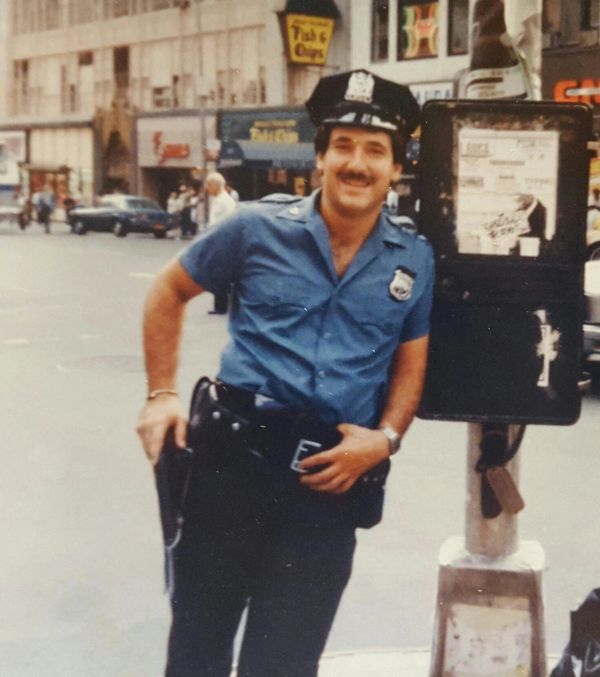 Smiling police officer leaning on a street sign.