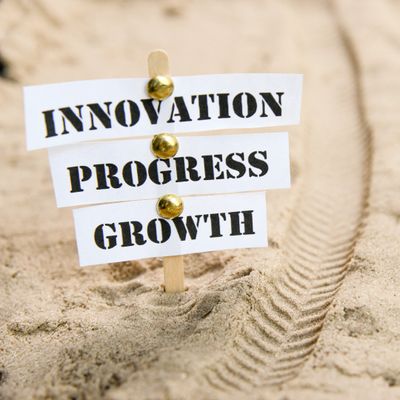 A sign that says innovation progress and growth in the sand.