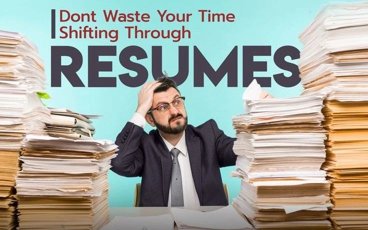 Photo shows Frustrated man overwhelmed by large stacks of resumes at work.