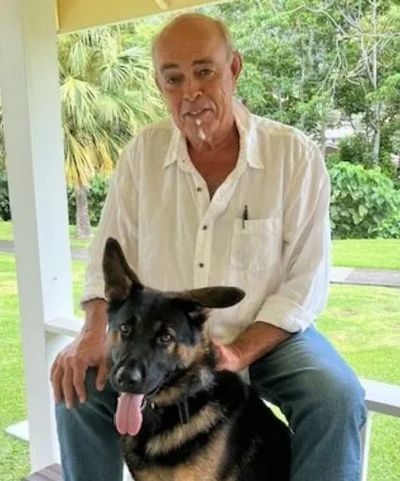 Man sitting on porch with a German Shepherd dog.