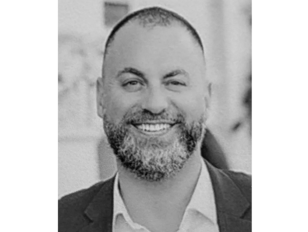 Smiling man with a beard wearing a blue suit jacket and white shirt.