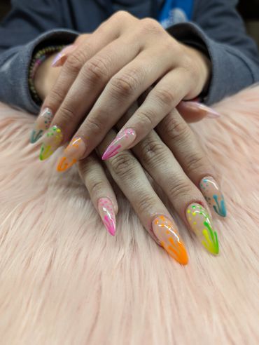 Colorful long nails with abstract designs on a soft pink surface.
