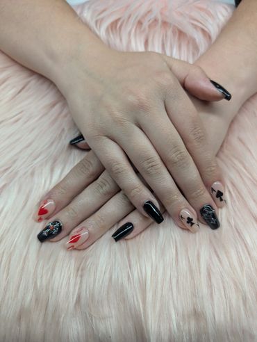 Hands with black and red artistic nail designs on a soft pink surface.
