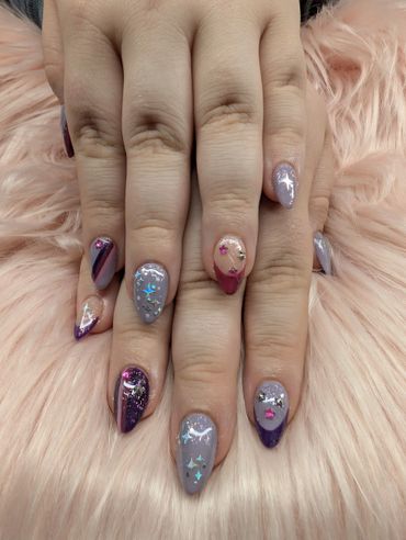 Stylish nails with purple and silver designs and star-shaped accents on a soft pink background.