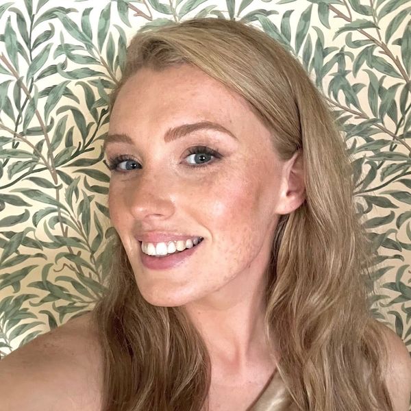 Smiling woman with light brown hair against leafy wallpaper.
