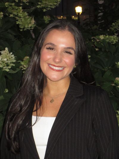 Smiling woman in a black blazer outdoors at night.