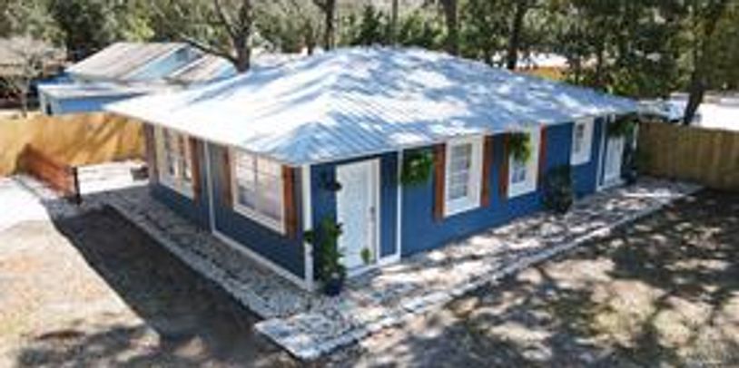 Blue single-story house with white roof and stone pathway in a shaded yard.