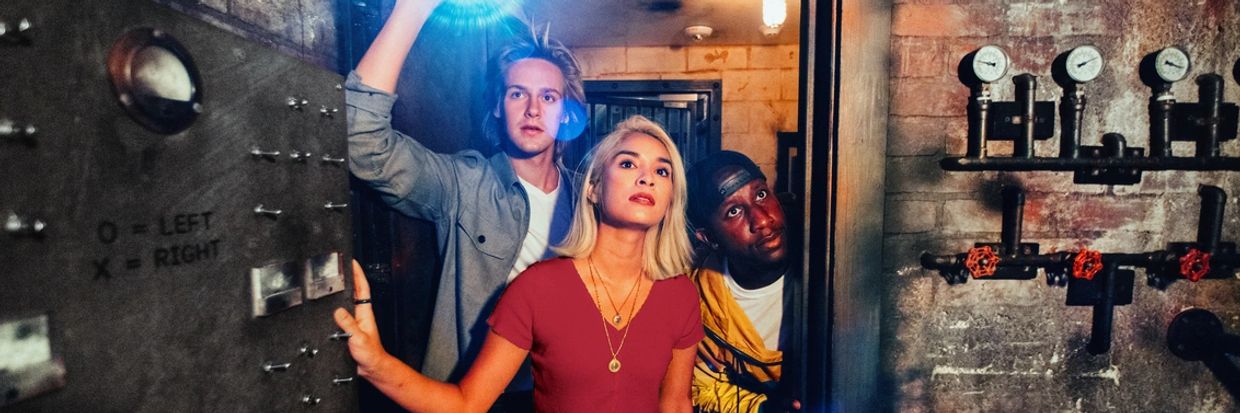 A stock photo of three people entering an escape room - one person is holding a flashlight.