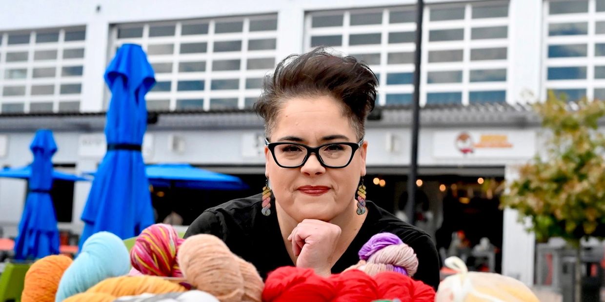 Person with glasses surrounded by colorful yarn balls.