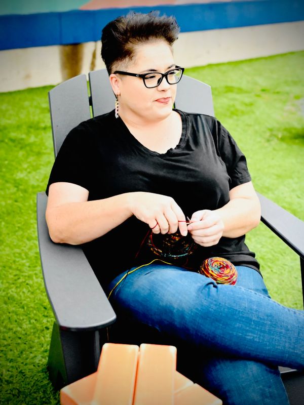 Woman knitting while sitting outdoors on a chair.