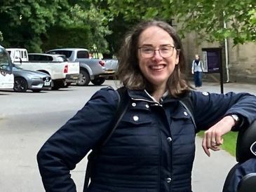 Woman smiling outdoors with glasses and a dark jacket.