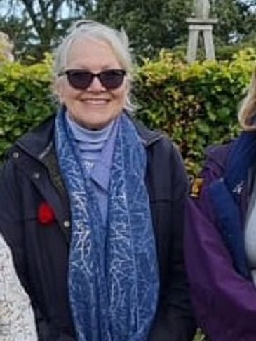 Smiling woman in sunglasses and blue scarf outdoors.