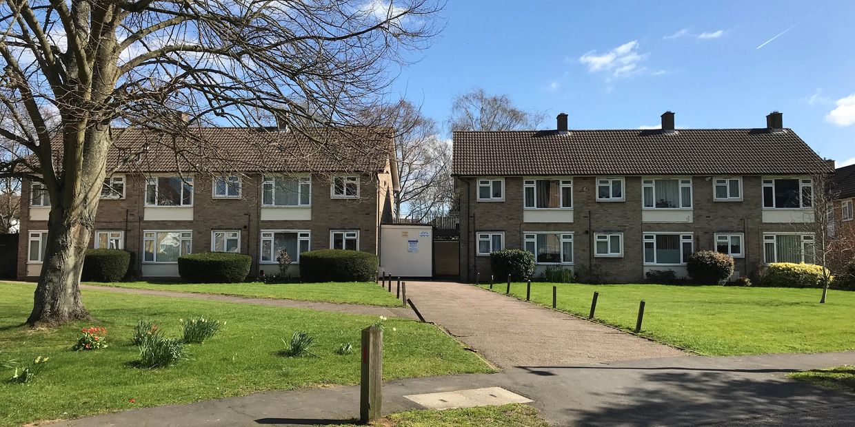 Two residential buildings with green lawns and a clear blue sky.