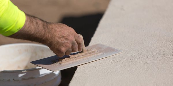 A hand smoothing cement with a trowel on a construction site.