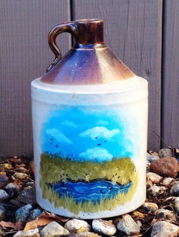 Ceramic jug with a hand-painted nature scene of a pond, grass, and birds.