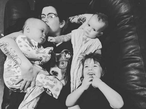 A person cuddles two babies and a young child on a couch in a black-and-white photo.