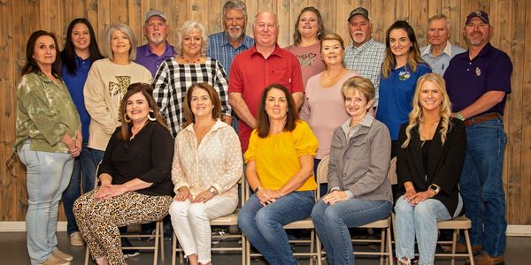 Group photo of 18 people posing indoors against a wooden backdrop.