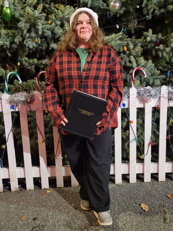 Young woman in a Santa hat holding a book in front of a Christmas tree.