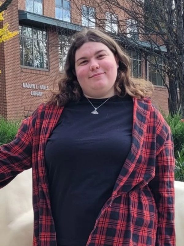 Smiling woman in a red plaid shirt outside a library.