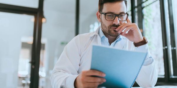 A man in glasses reads a blue document.