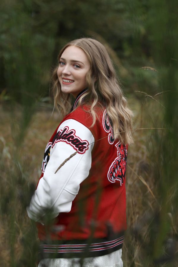 Young woman in a red and white Wildcats jacket smiles outdoors.